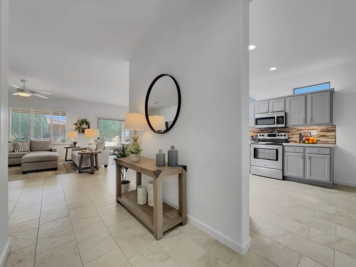 This scene looks into a bright living area with a round mirror, a console table with decorative items, a comfortable couch and seating area, and a view into the kitchen. The atmosphere is inviting, suggesting easy gatherings before heading out or returning from local adventures.