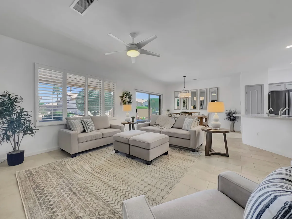 This image showcases a stylish and comfortable living space featuring light-colored sofas, a large window that allows natural sunlight to filter in, a decorative plant adding a fresh touch, and a dining area visible in the background. The open-plan layout creates a continuous flow between the living and dining spaces, highlighted by tasteful modern décor.