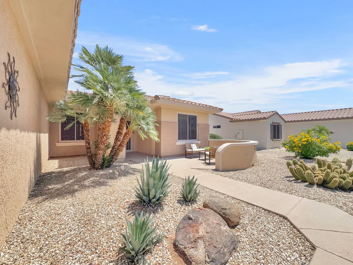 A tranquil exterior setting with a palm tree, inviting outdoor seating area, and desert landscaping. Rock features add texture, and the setting feels perfect for relaxing after activities or gathering with friends.