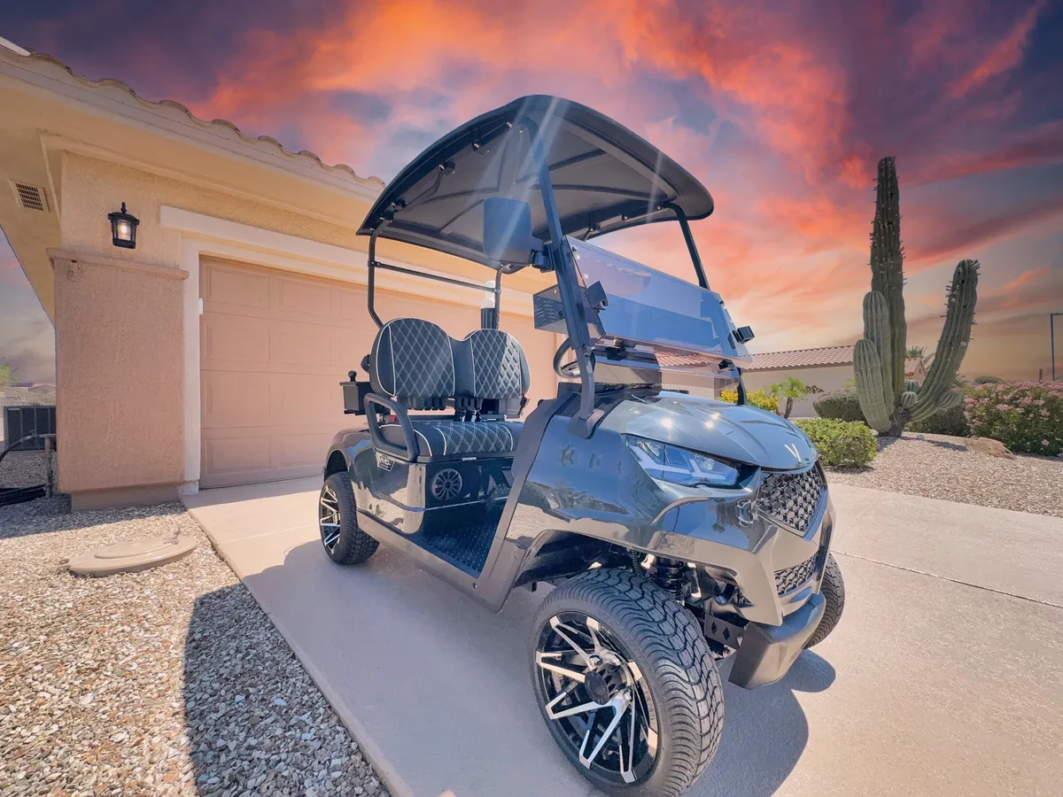 A golf cart is parked near desert plants under a colorful sky, evoking a sense of outdoor adventure and leisure. The landscape hints at the beauty of the surrounding community and the accessibility of golf and other outdoor amenities.