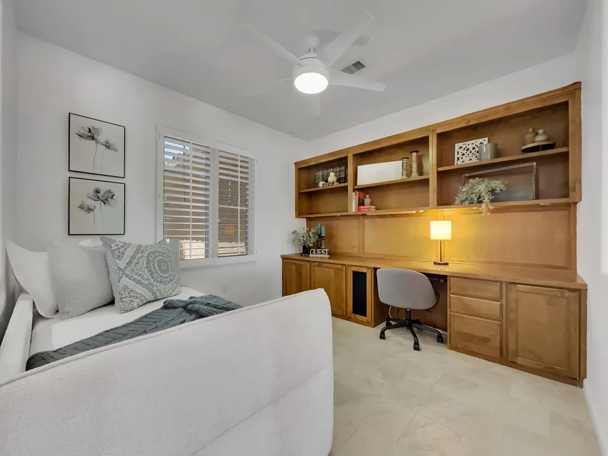 A dedicated office nook featuring a daybed, wooden shelving unit, and a desk with a lamp. The space is functional yet cozy, offering a quiet work environment and an extra sleeping option.