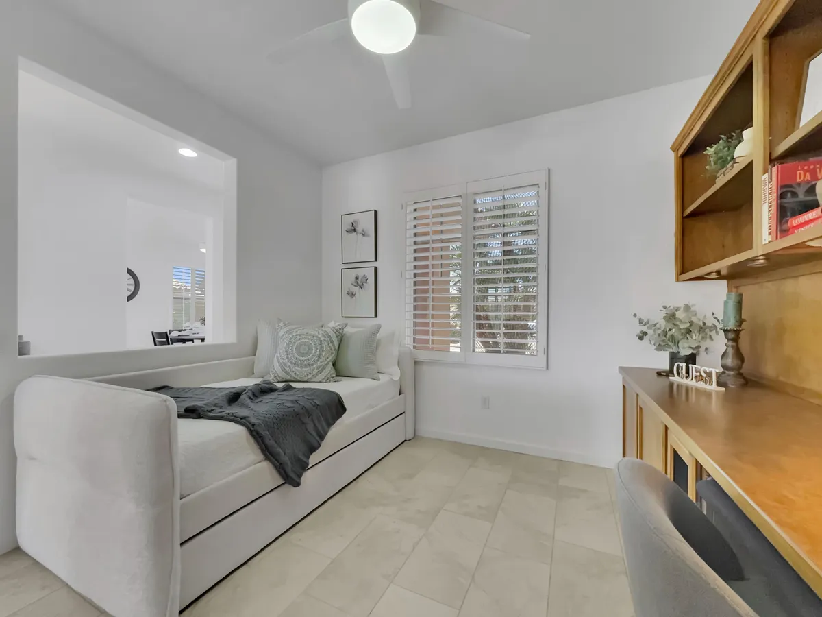 This image features a stylish daybed with decorative pillows and a wooden desk situated by a window with shutters. The space feels calm and comfortable, suggesting a multi-use area ideal for relaxing, reading, or working. Natural light streams in, creating an inviting environment for productivity and downtime.