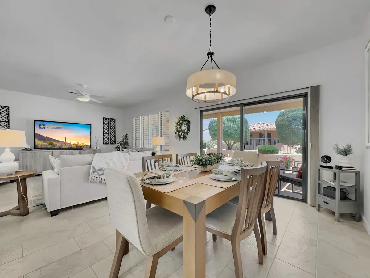 A welcoming scene featuring both a dining table and an adjacent cozy living area with a sofa, television, and large windows providing soft, natural light. The design is modern yet inviting, ideal for both social gatherings and quiet evenings.