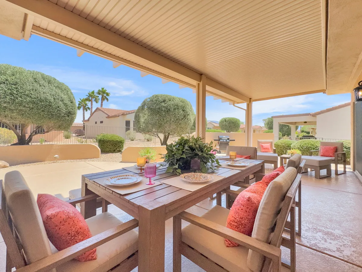 This image captures a beautifully arranged outdoor dining table surrounded by vibrant decorative cushions, lush landscaping, and an inviting BBQ grill set against palm trees. The setting evokes relaxed, social gatherings and highlights the backyard's alfresco dining appeal.